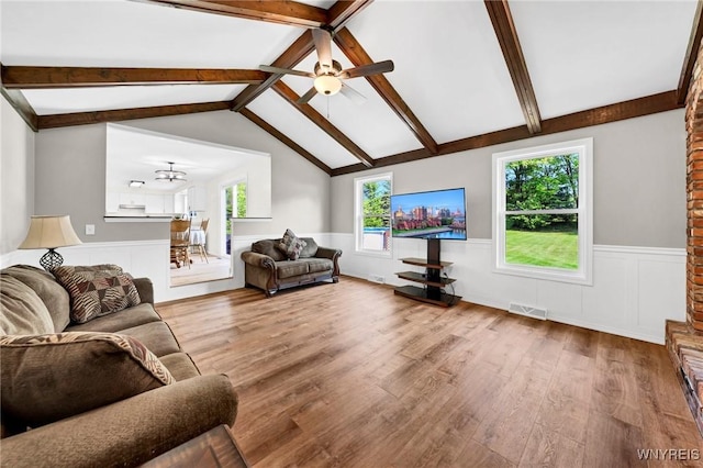 living area featuring vaulted ceiling with beams, wood finished floors, visible vents, a ceiling fan, and wainscoting