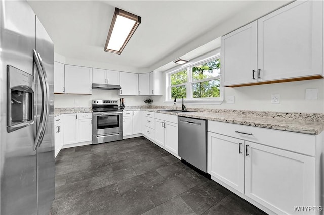 kitchen featuring white cabinets, light stone counters, stainless steel appliances, under cabinet range hood, and a sink