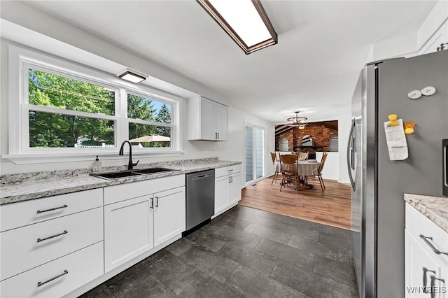 kitchen with light stone counters, appliances with stainless steel finishes, a sink, and white cabinetry