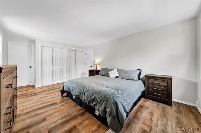 bedroom with baseboards, wood finished floors, and multiple closets