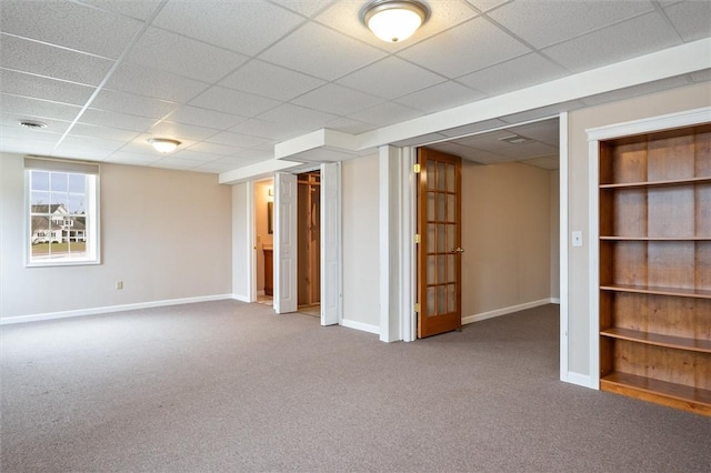 below grade area with a drop ceiling, carpet, and baseboards