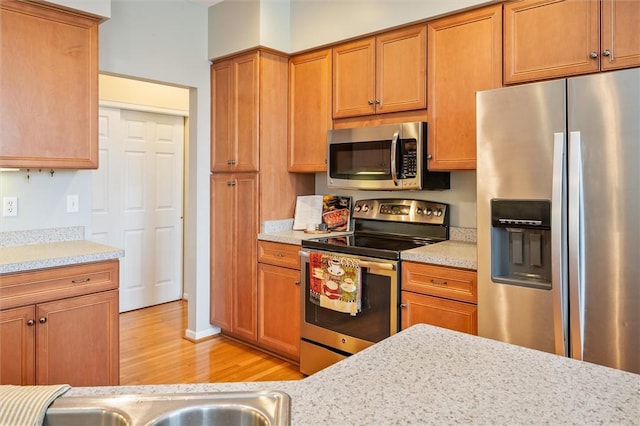 kitchen with appliances with stainless steel finishes, brown cabinetry, and light countertops