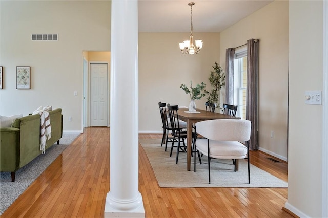 dining space with light wood-type flooring, visible vents, decorative columns, and a notable chandelier