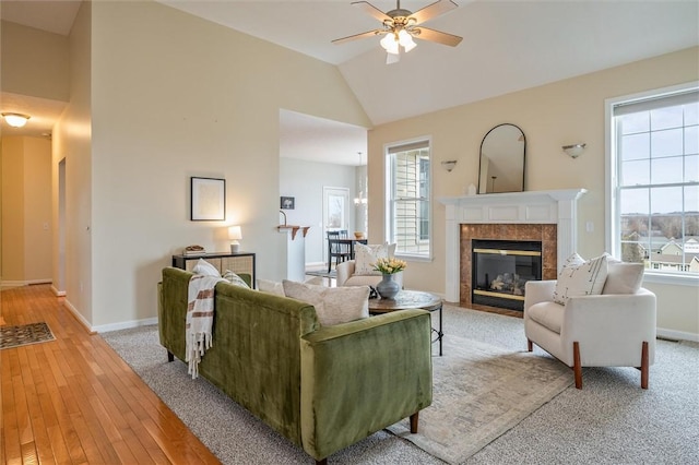 living area with ceiling fan, light wood-type flooring, a tiled fireplace, and baseboards