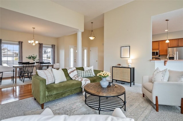 living area with baseboards, light wood-style floors, a towering ceiling, ornate columns, and a chandelier