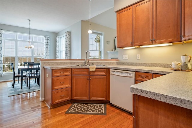 kitchen with brown cabinets, light wood-style floors, white dishwasher, a sink, and a peninsula