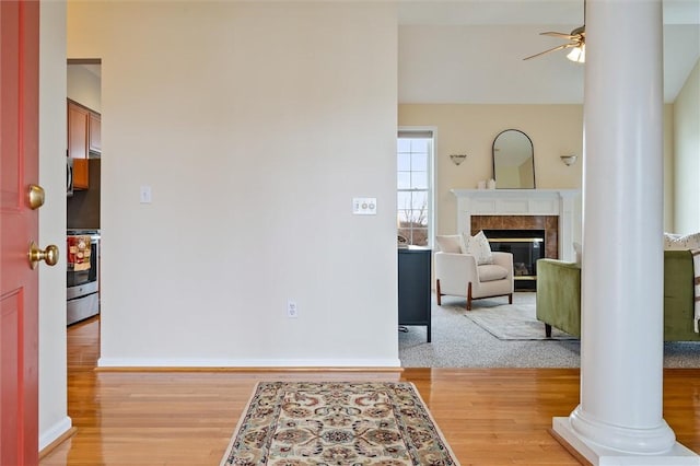 interior space featuring light wood-type flooring, ceiling fan, ornate columns, and a tile fireplace