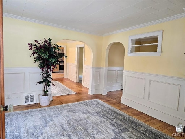 corridor with arched walkways, wainscoting, visible vents, and wood finished floors