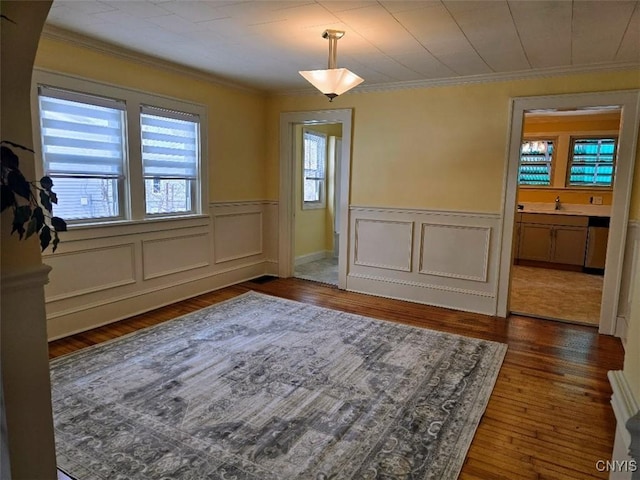 unfurnished dining area featuring a wainscoted wall, crown molding, a wealth of natural light, and wood finished floors