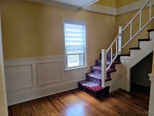 stairs featuring wainscoting, a decorative wall, wood-type flooring, and crown molding