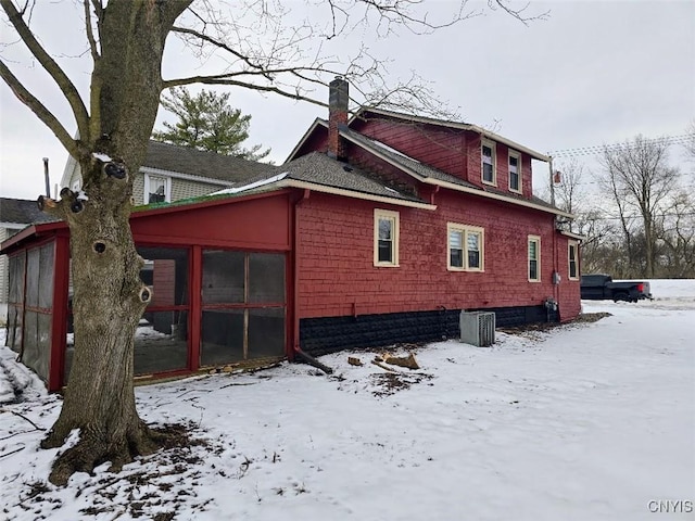 view of snow covered exterior with a chimney and a sunroom