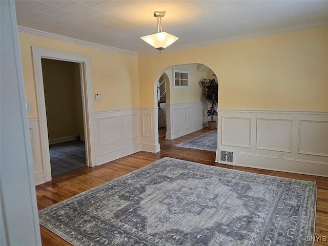 interior space featuring arched walkways, visible vents, ornamental molding, wainscoting, and wood finished floors