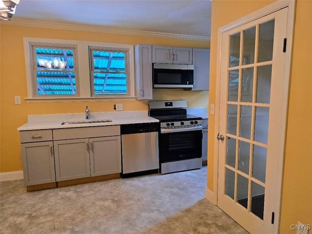 kitchen with gray cabinetry, stainless steel appliances, a sink, light countertops, and crown molding