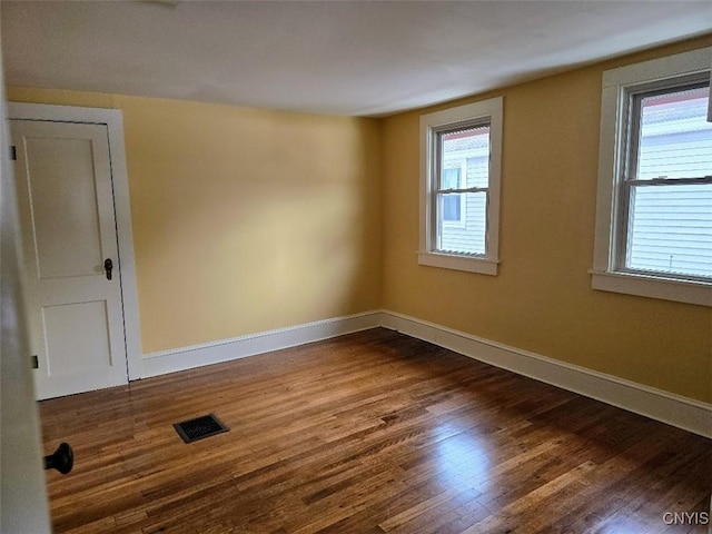 empty room with dark wood-type flooring, visible vents, and baseboards