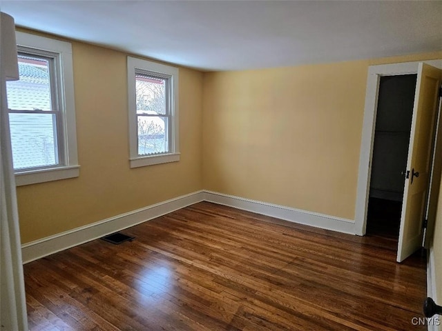 empty room with a healthy amount of sunlight, visible vents, baseboards, and dark wood finished floors