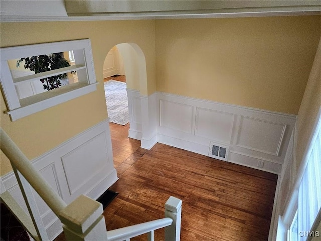 interior space with visible vents, arched walkways, dark wood finished floors, a wainscoted wall, and a decorative wall