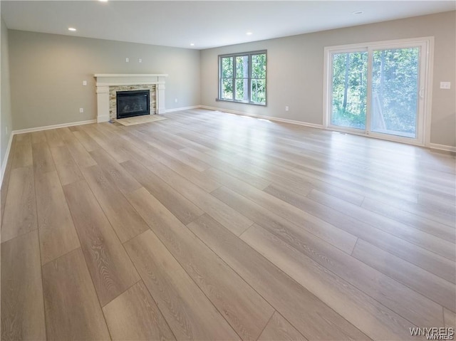 unfurnished living room with a fireplace with flush hearth, recessed lighting, baseboards, and light wood finished floors