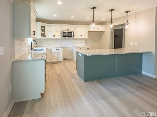 kitchen featuring light wood-style flooring, a sink, stainless steel microwave, light stone counters, and a peninsula