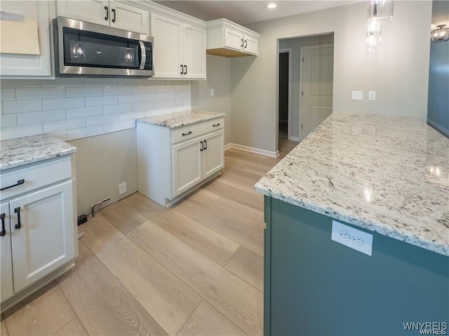 kitchen with tasteful backsplash, stainless steel microwave, light wood-style flooring, and light stone counters