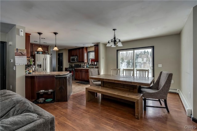 dining room featuring a chandelier, baseboard heating, wood finished floors, and baseboards