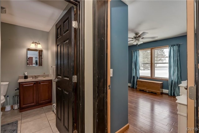 bathroom featuring a baseboard radiator, toilet, ceiling fan, vanity, and baseboards