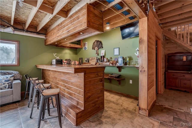 bar with a bar, stone finish flooring, and baseboards