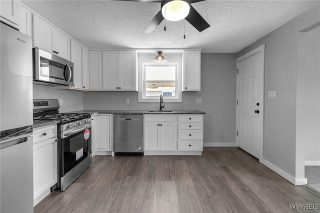 kitchen with appliances with stainless steel finishes, white cabinets, a sink, and dark wood-style floors