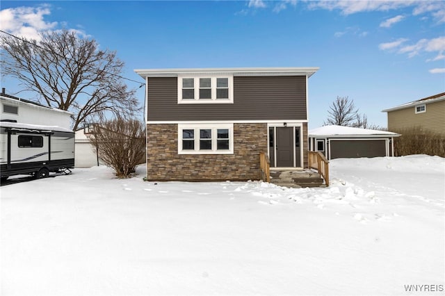 snow covered property featuring a garage, stone siding, and an outdoor structure