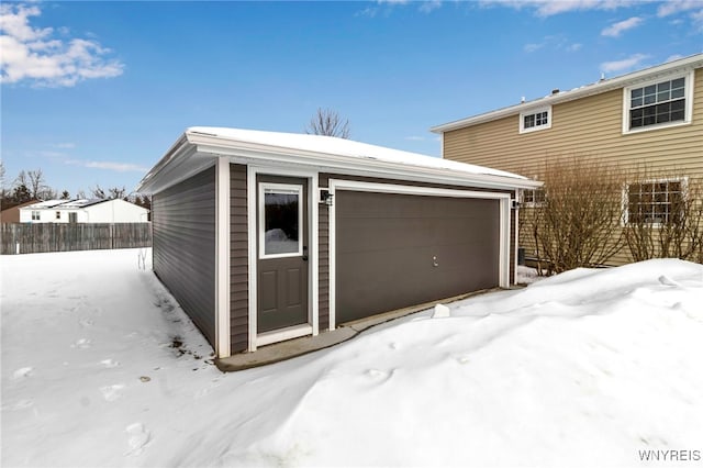 snow covered garage featuring a garage and fence