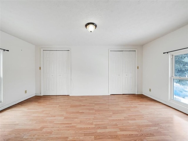 unfurnished bedroom featuring light wood-type flooring, a textured ceiling, baseboards, and two closets