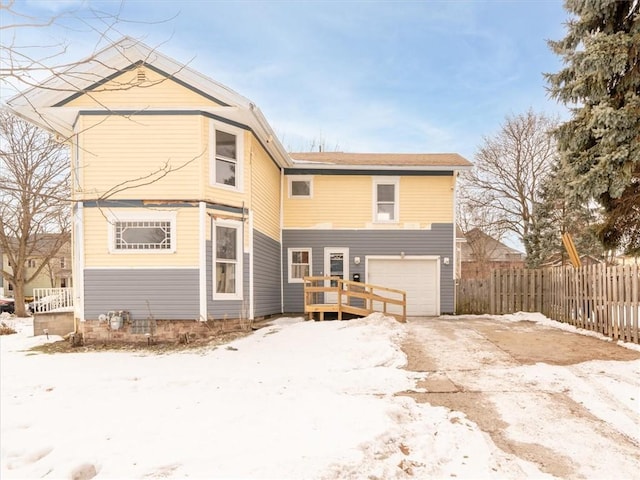 snow covered rear of property with an attached garage and fence