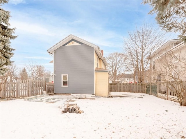 snow covered house featuring a chimney and fence