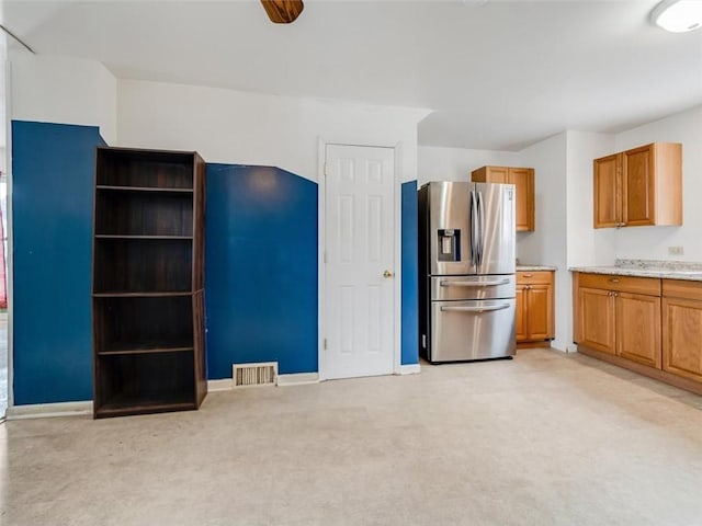 kitchen with brown cabinets, light countertops, visible vents, light carpet, and stainless steel fridge