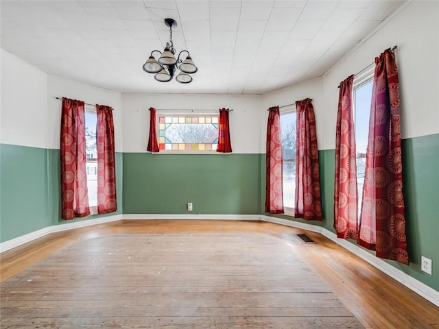 spare room featuring visible vents, baseboards, hardwood / wood-style flooring, and a notable chandelier