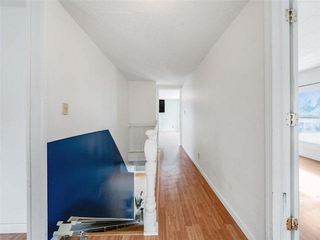 hallway with a textured ceiling, wood finished floors, and baseboards