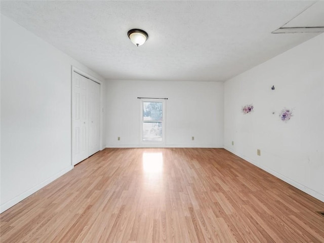 unfurnished room featuring a textured ceiling, light wood finished floors, and baseboards