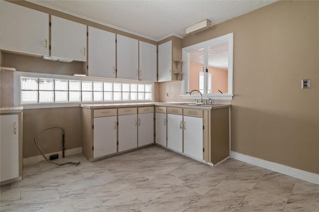 kitchen featuring marble finish floor, light countertops, a sink, and baseboards