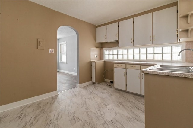 kitchen with baseboards, arched walkways, marble finish floor, light countertops, and a sink