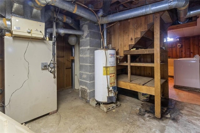 unfinished below grade area featuring concrete block wall, gas water heater, heating unit, wooden walls, and independent washer and dryer