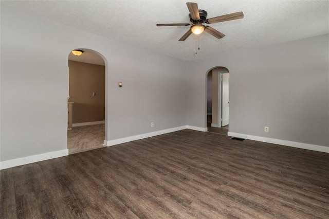 spare room featuring baseboards, arched walkways, and dark wood-style flooring