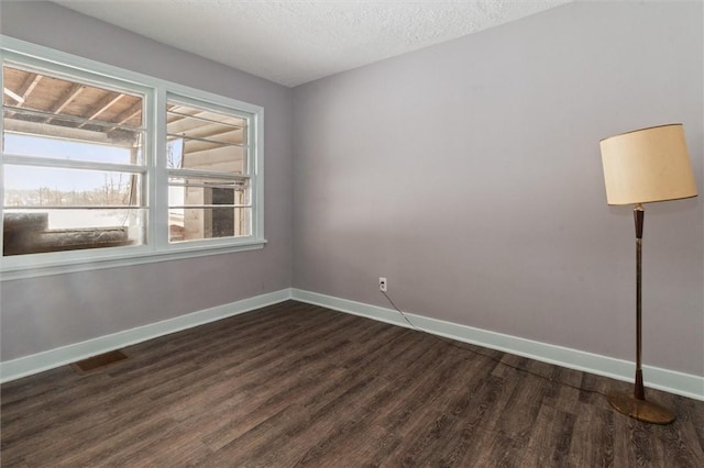 spare room with visible vents, baseboards, dark wood finished floors, and a textured ceiling