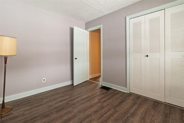 unfurnished bedroom with dark wood-style flooring, a closet, visible vents, a textured ceiling, and baseboards