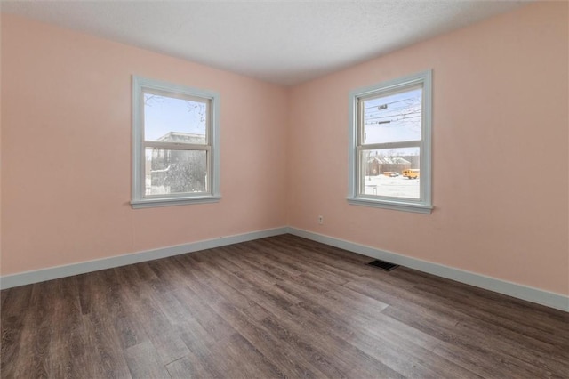 spare room with dark wood-style floors, plenty of natural light, visible vents, and baseboards