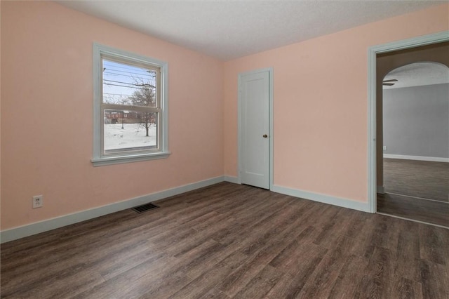 empty room with arched walkways, dark wood-style flooring, visible vents, and baseboards