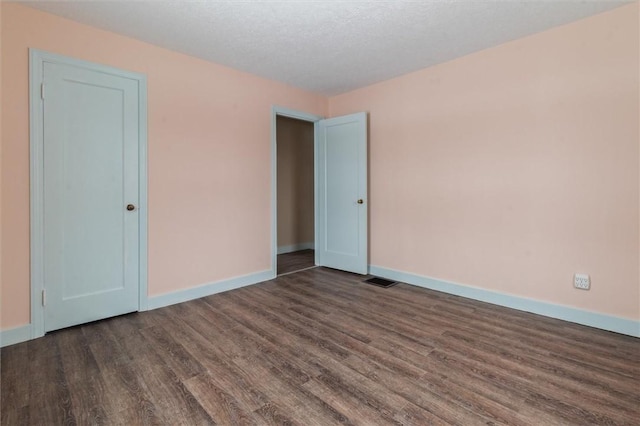 unfurnished room with visible vents, dark wood finished floors, a textured ceiling, and baseboards