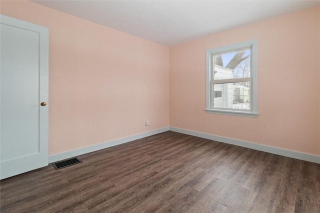 spare room with dark wood-type flooring, visible vents, and baseboards