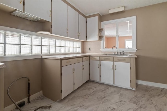 kitchen featuring marble finish floor, a sink, light countertops, and white cabinets