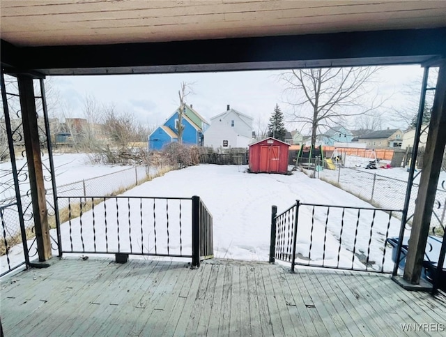 snow covered deck with an outbuilding, fence, and a storage unit