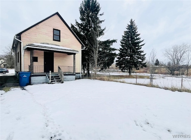 snow covered rear of property featuring covered porch and fence