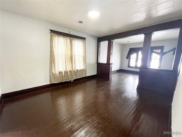 unfurnished room featuring ornate columns, visible vents, baseboards, and hardwood / wood-style flooring